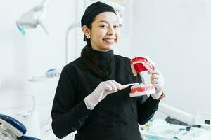 Smiling female dentist showing a denture, Dentist explaining tooth brushing, female dentist showing a denture and brush photo