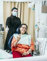 Dentist with thumb up patient in office, Woman shows thumb up sitting in dentist office, Dentist and satisfied patient with thumb up photo