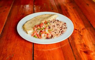 Gallopinto dish with quesillo and pico de gallo on wooden table. Traditional Gallo Pinto Meal with Pico de Gallo and quesillo served photo