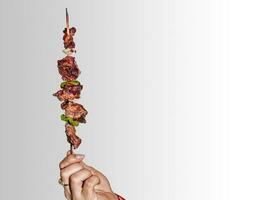 A hand holding a roast beef skewer, Hand holding roast beef skewer on white background photo