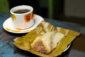 ver de un relleno tamal con un taza de café servido en un de madera mesa, tradicional tamal pisque relleno con un taza de café servido en el mesa. tamal pisque relleno típico nicaragüense comida foto