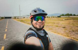 contento ciclista con lentes y casco tomando un autofoto yo retrato de contento masculino ciclista al aire libre foto