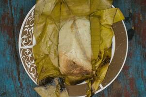Traditional Tamal Pisque stuffed in banana leaf served on wooden table, Central American typical food Tamal Pisque stuffed. Stuffed tamale served on wooden table photo