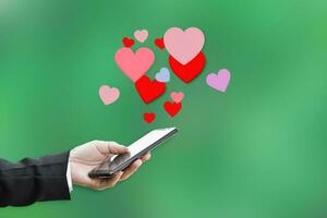 Male hands holding mobile phone with hearts, Love symbol on green background. Valentine's day concept. photo