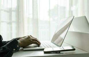 Man's hands using laptop computer with smartphone on white table at home. Online shopping, home work, freelance, online learning concept. photo