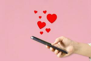 Female hands holding mobile phone with hearts, Love symbol on pink background. Valentine's day concept. photo