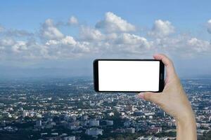 mano participación teléfono inteligente blanco pantalla terminado azul cielo nube y ciudad. foto