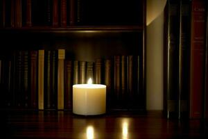 A Lit Candle On A Table In Front Of A Bookshelf. AI Generated photo