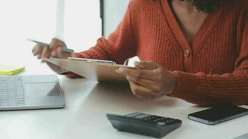 encantadora joven mujer de negocios asiática sentada en una computadora portátil en la oficina, haciendo un informe que calcula el documento de verificación del servicio de ingresos internos del saldo. video