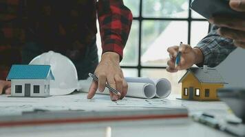 squadra di multietnico architetti Lavorando su costruzione piani nel incontro camera. ingegneri discutere su progetto nel ufficio. maturo uomo d'affari e donna in piedi in giro tavolo Lavorando su planimetria. video