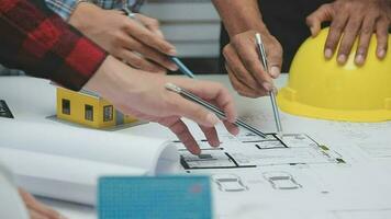 squadra di multietnico architetti Lavorando su costruzione piani nel incontro camera. ingegneri discutere su progetto nel ufficio. maturo uomo d'affari e donna in piedi in giro tavolo Lavorando su planimetria. video