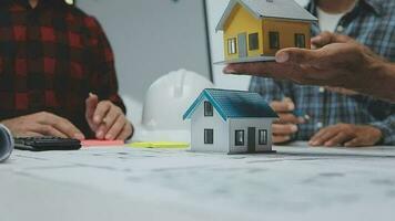 team van multi-etnisch architecten werken Aan bouw plannen in vergadering kamer. ingenieurs bespreken Aan project in kantoor. volwassen zakenman en vrouw staand in de omgeving van tafel werken Aan blauwdruk. video