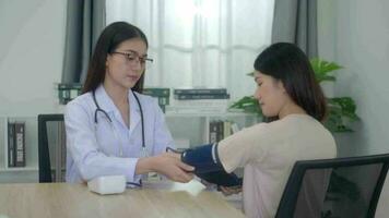 un hembra asiático médico medidas asiático mujer sangre presión durante un médico consulta en clínica oficina. video