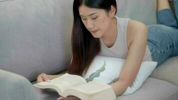 Asian young woman reading book on sofa lying in a relaxed position at home. video