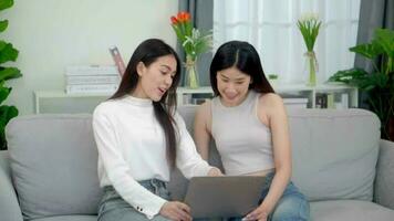 samenspel gelukkig Aziatisch Dames het beste vrienden lachend terwijl werken met laptop Bij huis. video