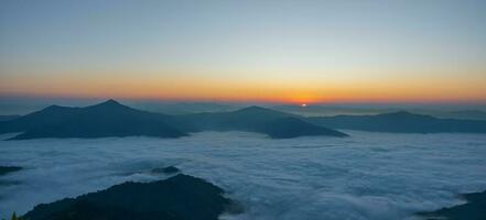 Beautiful landscape on the mountains at sunrise. Spectacular view in foggy valley covered forest under morning sky. photo