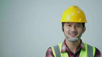 Asian young engineer wearing a yellow safety goggles and safety vest. looking to the side and smiling. Isolated on a white backdrop. video