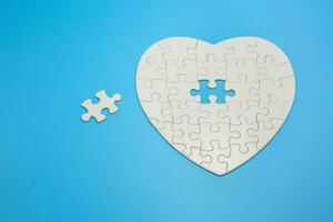 White heart shaped jigsaw puzzle on blue background with copy space. Business strategy teamwork and problem solving concept. photo