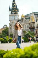 Happy hipster woman with sunglasses having fun. Girl smiling with casual clothes, emotional moment. City square with historical architectural buildings. Tower on square in Batumi city in Georgia. photo
