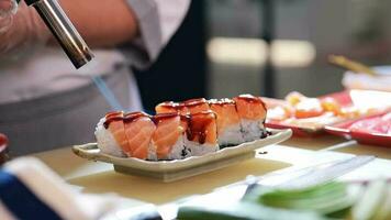 Close-up 4K slow-motion video of salmon sushi making. The sauce is poured, followed by the flame burning from flames gun on the surface of of the salmon sushi.