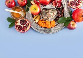 A dish with a New Year's treat for the holiday Rosh Hashanah. pomegranate, honey, dates, apple slices and carrots. Blue background. A copy space. photo