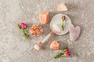 Top view of quartz roller and gua sha on a white round marble stand and rosebuds and lumps of salt. The concept of spa, relaxation. cement background. photo