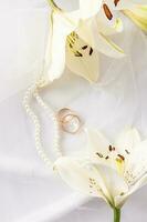 Chic vertical wedding background for design, layout, postcard, invitation. two gold wedding rings, a string of pearls and white lilies. photo