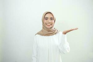 Smiling young Asian muslim woman in wearing casual clothes showing copy space on palm on white background photo