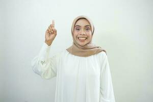 Amazed young Asian woman in white shirt pointing finger up at copy space isolated over white background photo