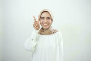 alegre joven asiático mujer en blanco vestir demostración paz firmar terminado ojos aislado terminado blanco antecedentes foto