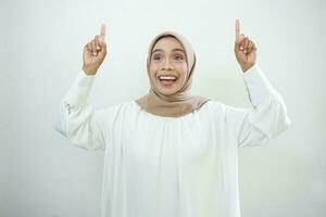 Amazed young Asian woman in white shirt pointing finger up at copy space isolated over white background photo