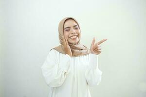 Cheerful beautiful Asian woman in white dress pointing fingers aside at copy space isolated over white background photo