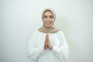 joven asiático islam mujer vistiendo Pañuelo da saludo manos a con un grande sonrisa en su rostro. indonesio mujer en gris antecedentes. eid mubarak, eid fitr, Ramadán foto