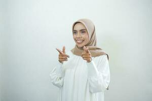 Cheerful beautiful Asian woman in white dress pointing fingers aside at copy space isolated over white background photo
