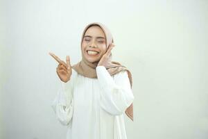 Cheerful beautiful Asian woman in white dress pointing fingers aside at copy space isolated over white background photo