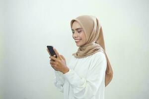 Beautiful smiling Asian Muslim woman wearing hijab Using mobile phone, typing sms message isolated on white background studio portrait. People religious lifestyle concept photo