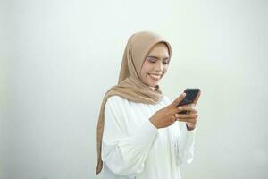 Beautiful smiling Asian Muslim woman wearing hijab holding mobile phone in hand isolated on white background studio portrait. People religious lifestyle concept photo