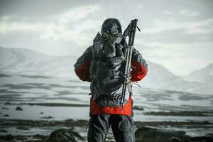 Men with Backpack and Trekking Poles Facing Extreme Wilderness Conditions Ahead of Him. photo