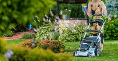 Gardener Worker Trimming Grass Using Electric Mower photo