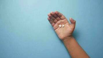 ein Hand mit zwei Weiß Tabletten auf ein Blau Hintergrund video