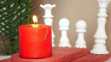 a red candle sits on a wooden table next to a chess board video