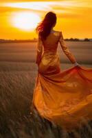 Young woman in yellow dress walking through wheat field at sunset. photo