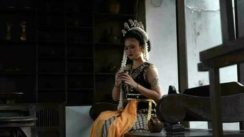 a Javanese bride is drinking a cup of tea in the living room with brown wooden chairs video