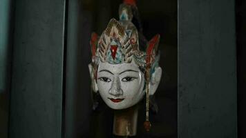 a wooden doll called wayang is white and wears a crown in a traditional cupboard video
