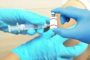 Closeup hand doctor showing vial vaccine development and creation of a coronavirus vaccine COVID-19 and blurry test injection patient background. photo