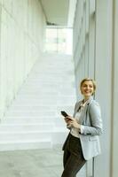 Businesswoman using mobile phone on modern office hallway photo