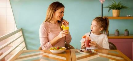 madre y hija teniendo un desayuno con Fresco exprimido jugos en el café foto