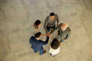 Group of young and senior business people come together in an office hallway, standing in a circle with their hands joined photo