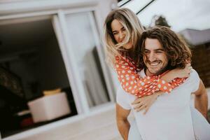 Handsome long hair man carrying the young woman on his back in front of brick house photo
