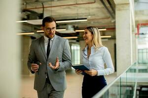 Young coworkers walking and talking along corridor in modern office photo